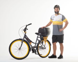 Imagem de um entregador ciclista da Mobi Logística, utilizando o uniforme e ao lado de uma bicicleta da marca.