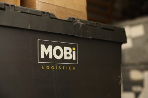 Imagem de um recipiente da Mobi Logística, com algumas caixas de papelão acima dele.