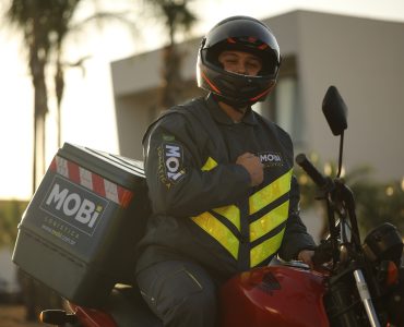 magem de um entregador ciclista da Mobi Logística, utilizando o uniforme e ao lado de uma bicicleta da marca.