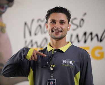 Funcionário da Mobi sorrindo e apontando para o logo da Mobi presente em seu uniforme.