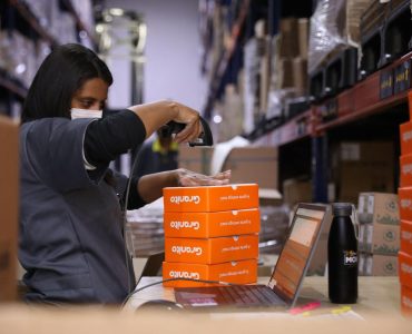 Funcionária da Mobi utilizando um coletor de dados de estoque para coletar informações de algumas caixas laranjas no armazém da empresa.