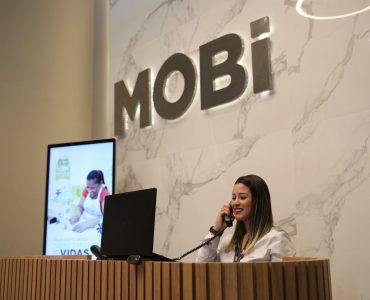 Recepcionista da Mobi falando ao telefone. Ao fundo, o logo da marca.