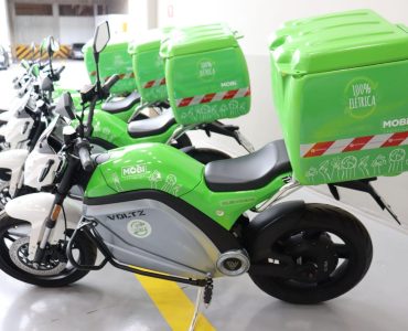 5 motos elétricas verdes da Mobi logística, com baú verde na traseira.