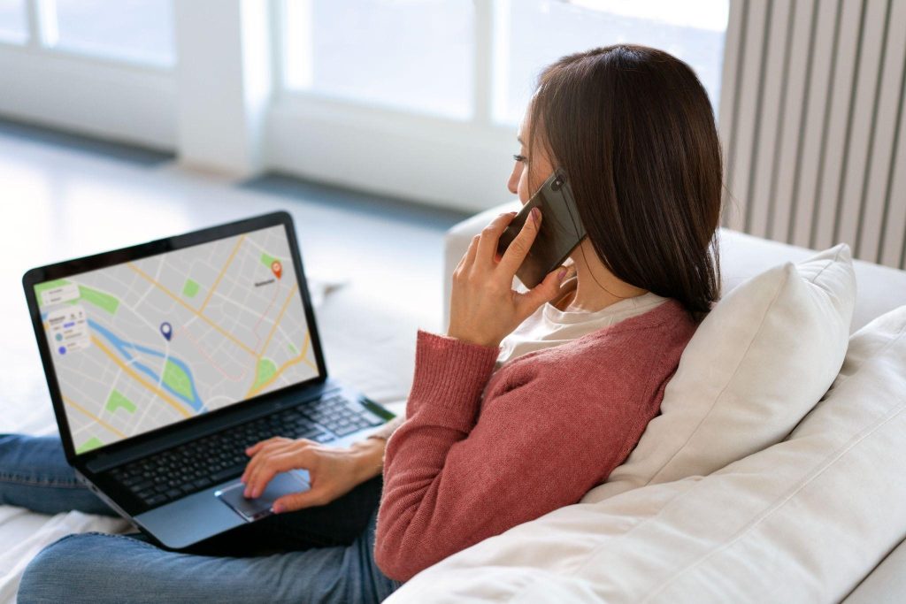 Mulher sentada no sofá falando no telefone olhando para tela do notebook com mapa de rastreamento.