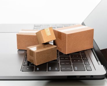 Pequenas caixas de papelão sobre o teclado de um laptop aberto, simbolizando compras online e entrega de encomendas.